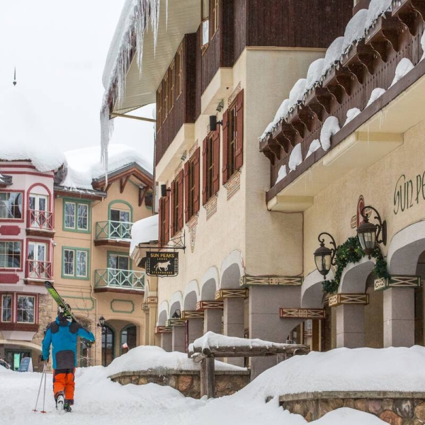 Skiers with gear over their shoulders walk through the snow-covered village at Sun Peaks Resort.