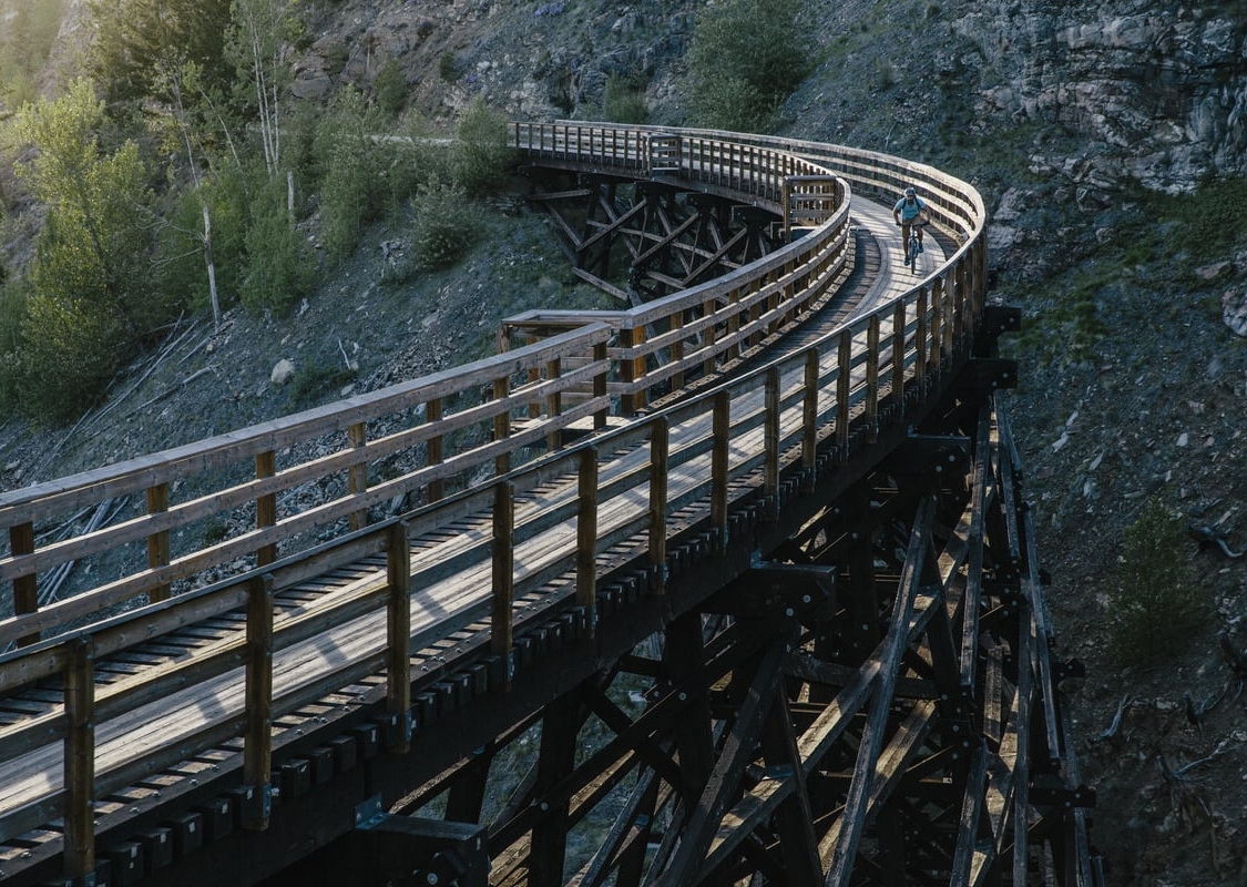 A wooden trestle bridge enters from the bottom left of the frame, and curves around and out the top left with a rocky bluff behind it