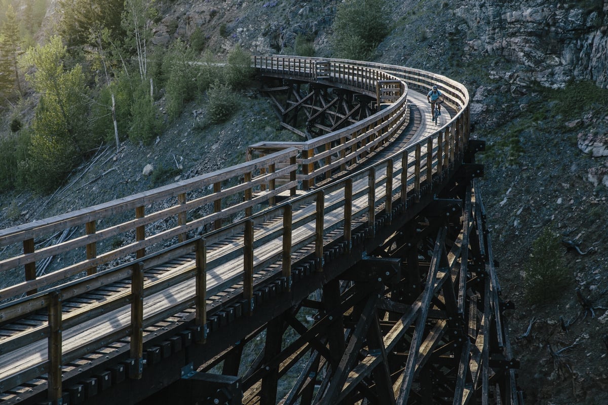 A wooden trestle bridge enters from the bottom left of the frame, and curves around and out the top left with a rocky bluff behind it