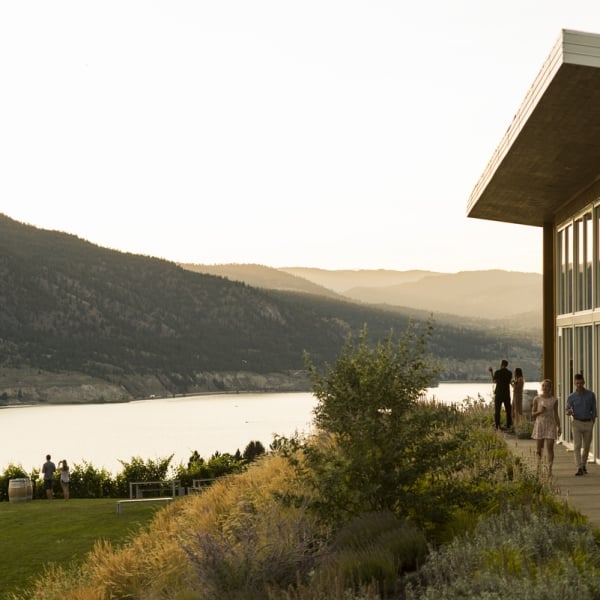 Outside shot of the Poplar Grove Winery with people walking alongside the glass walls. The winery overlooks a lake.