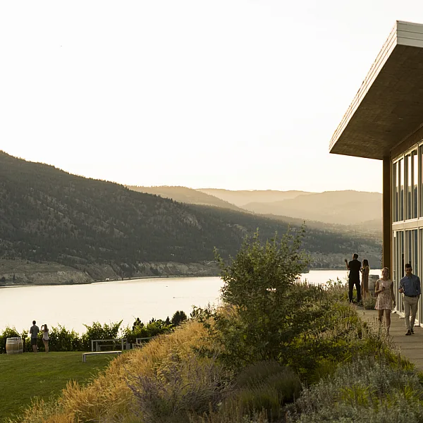 Outside shot of the Poplar Grove Winery with people walking alongside the glass walls. The winery overlooks a lake.