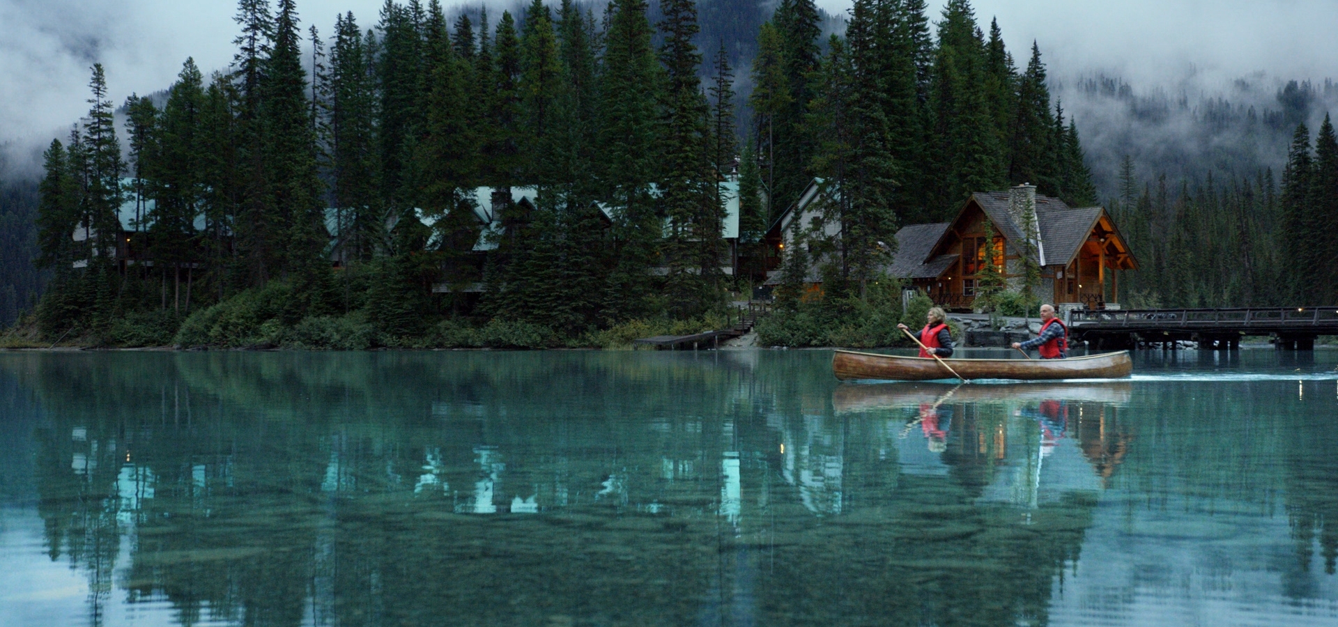 Yoho National Park - Emerald Lake. Wide static slow motion shot of couple canoeing on calm lake past lodge