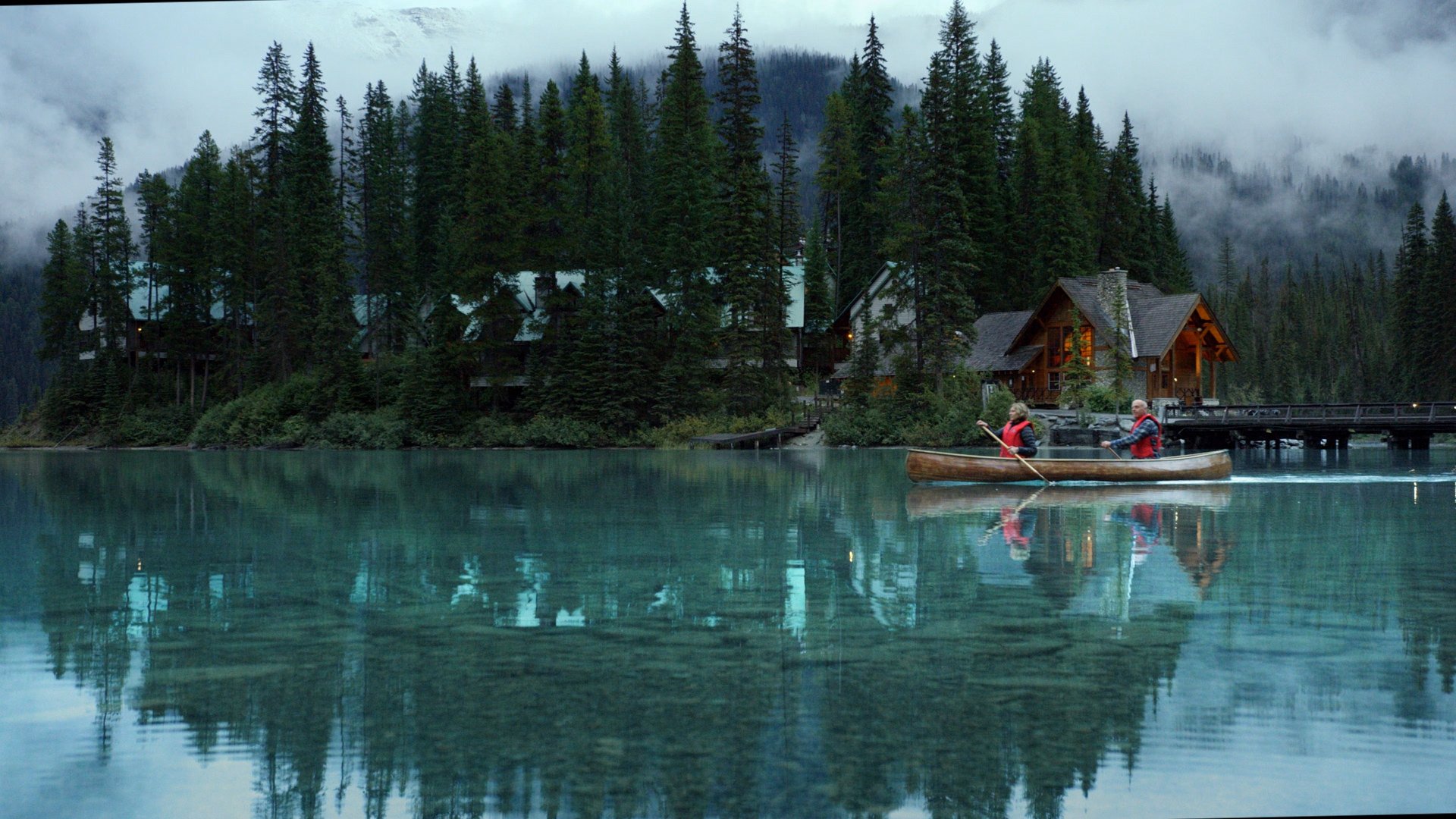 Yoho National Park - Emerald Lake. Wide static slow motion shot of couple canoeing on calm lake past lodge