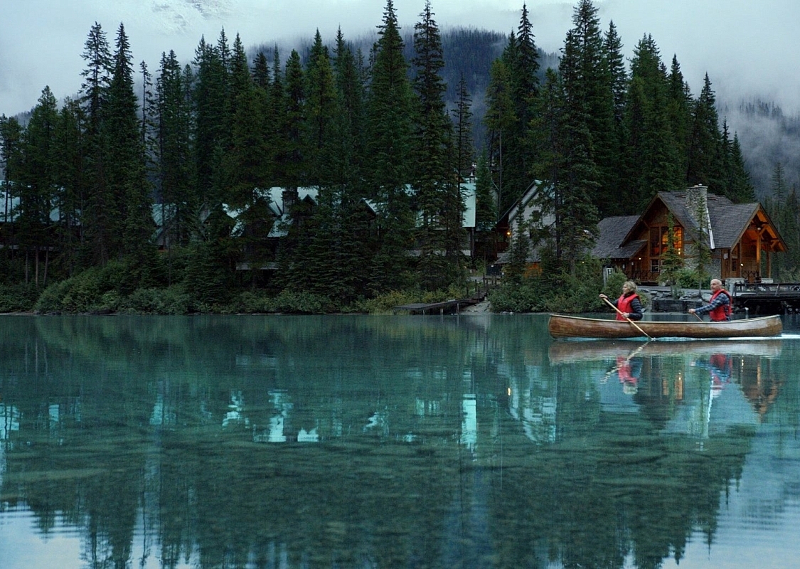 Yoho National Park - Emerald Lake. Wide static slow motion shot of couple canoeing on calm lake past lodge