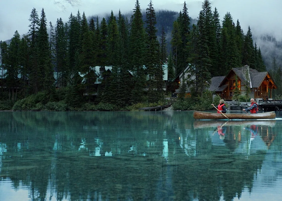 Yoho National Park - Emerald Lake. Wide static slow motion shot of couple canoeing on calm lake past lodge