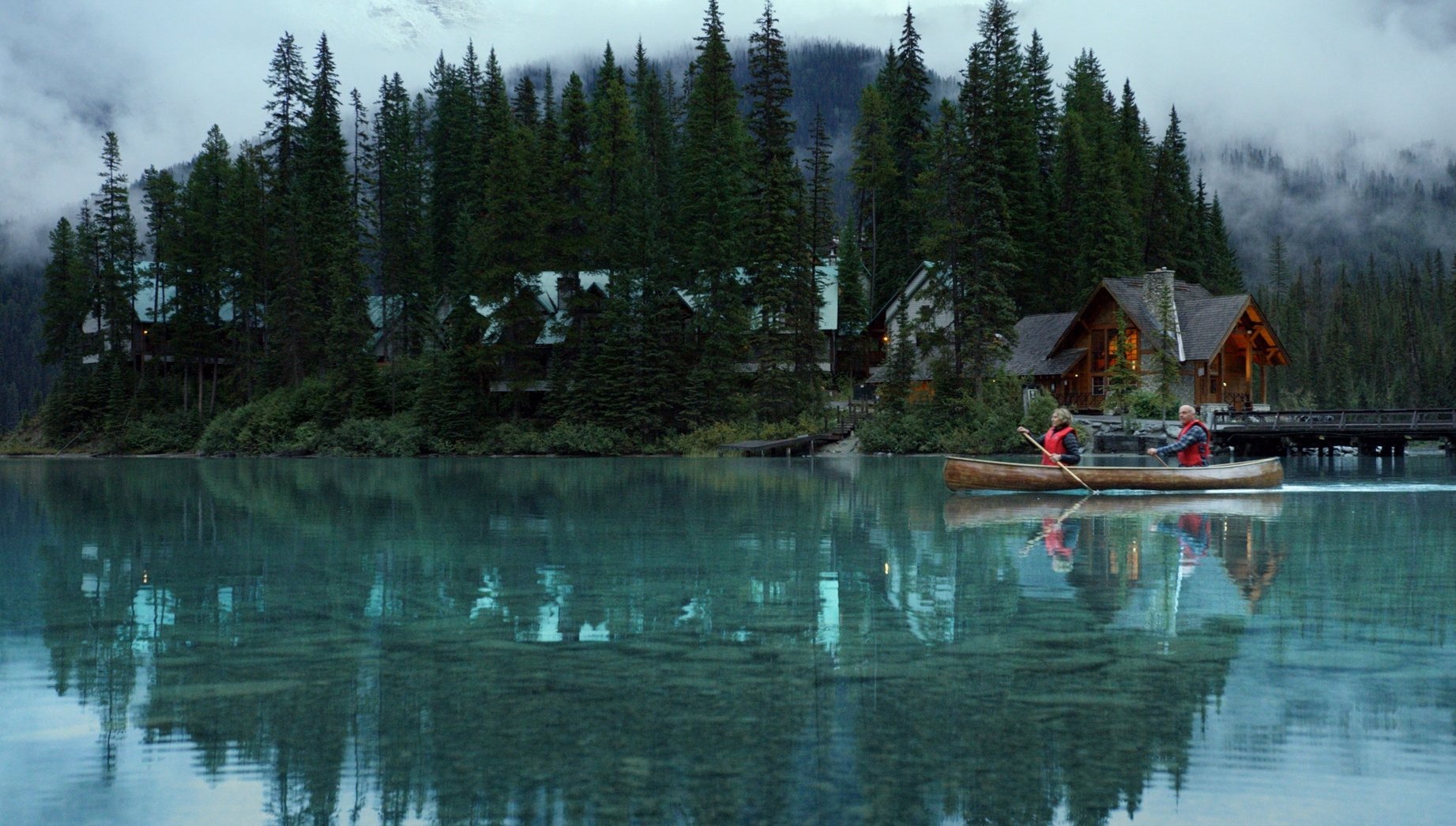 Yoho National Park - Emerald Lake. Wide static slow motion shot of couple canoeing on calm lake past lodge