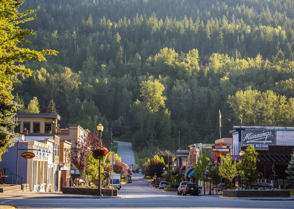 Downtown Revelstoke from street level. Shops line the street with green trees heading up the mountains behind.