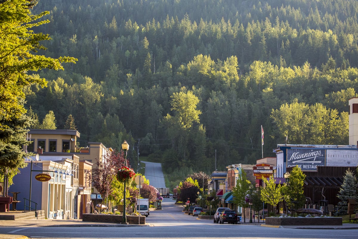 Downtown Revelstoke from street level. Shops line the street with green trees heading up the mountains behind.