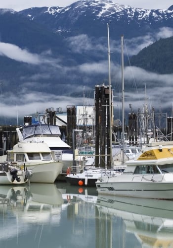 Boats in the harbour on a sunny day at the Bella Coola Marina, mountains behind with a touch of snow at the peaks