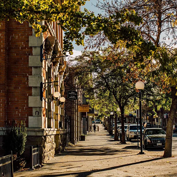 The corner of a brick building is on the left of a tree-lined sidewalk in downtown Kamloops.