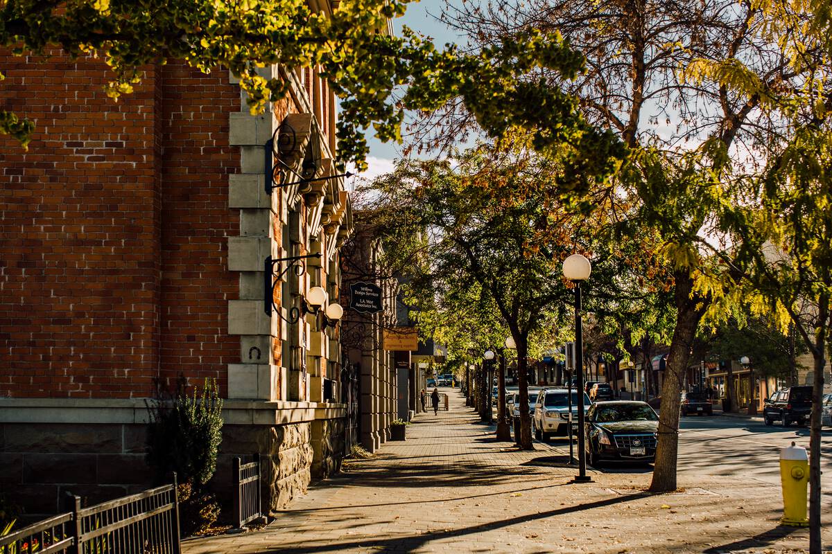 The corner of a brick building is on the left of a tree-lined sidewalk in downtown Kamloops.