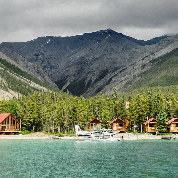 Northern Rockies Lodge mit kleinen Hütten am See, Bergblick und einem davor geparkten Wasserflugzeug.
