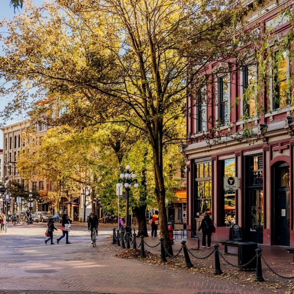 People crossing the street with a heritage brick building on the right with tall, leafy trees in front