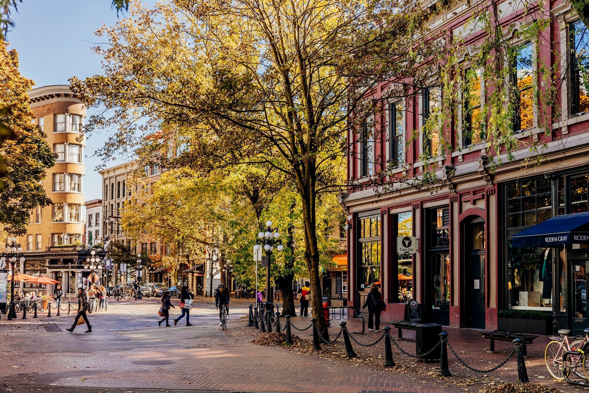 People crossing the street with a heritage brick building on the right with tall, leafy trees in front