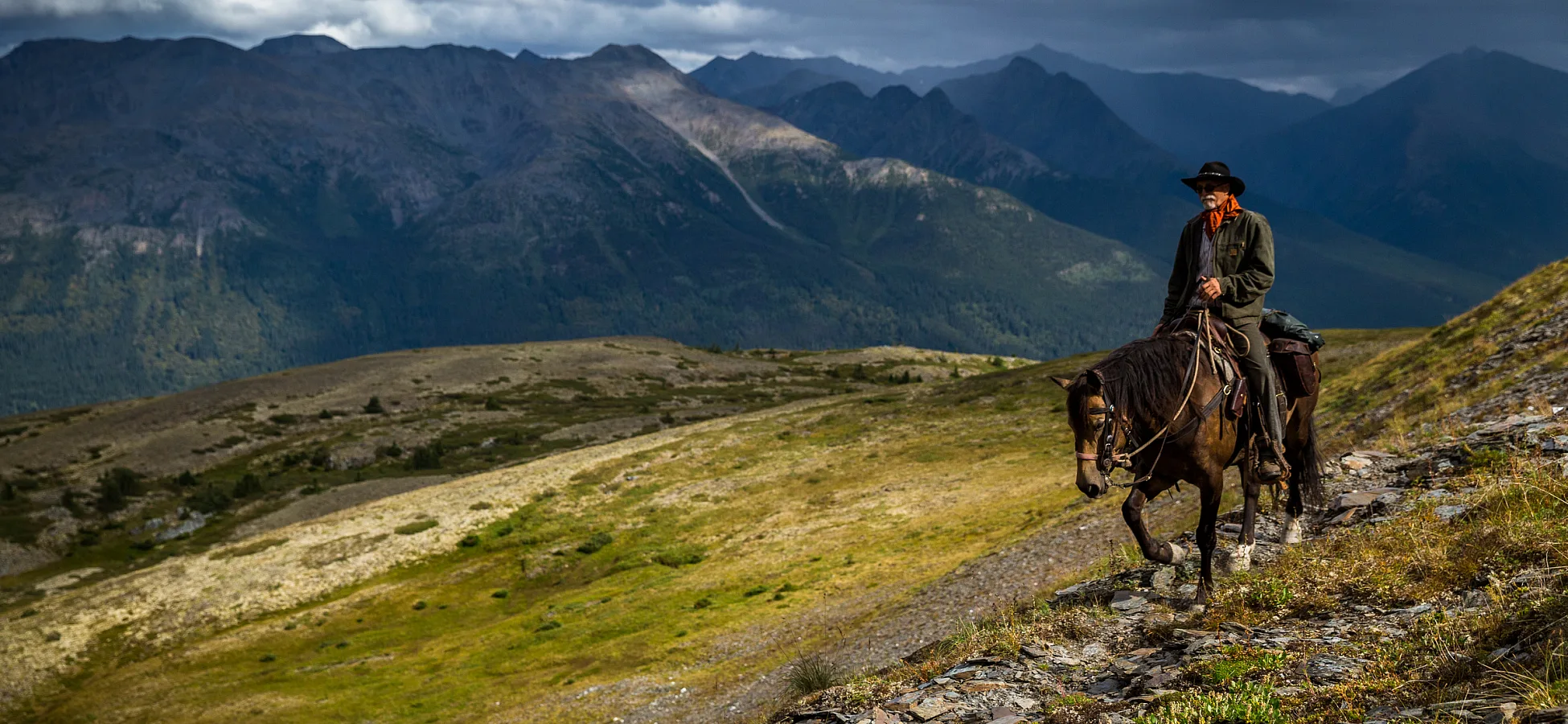 A lone horseback rider traverses the rugged countryside with rocks, sparse foliage and mountains as far as the eye can see.