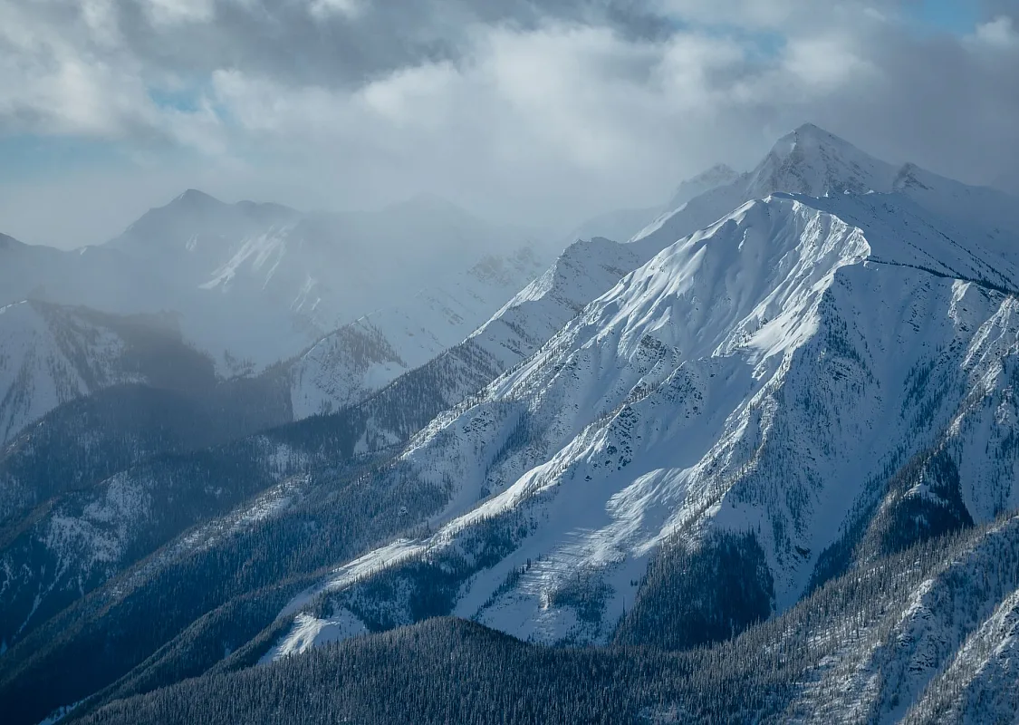 Aerial view of imposing, snow-covered mountains with a foggy sky
