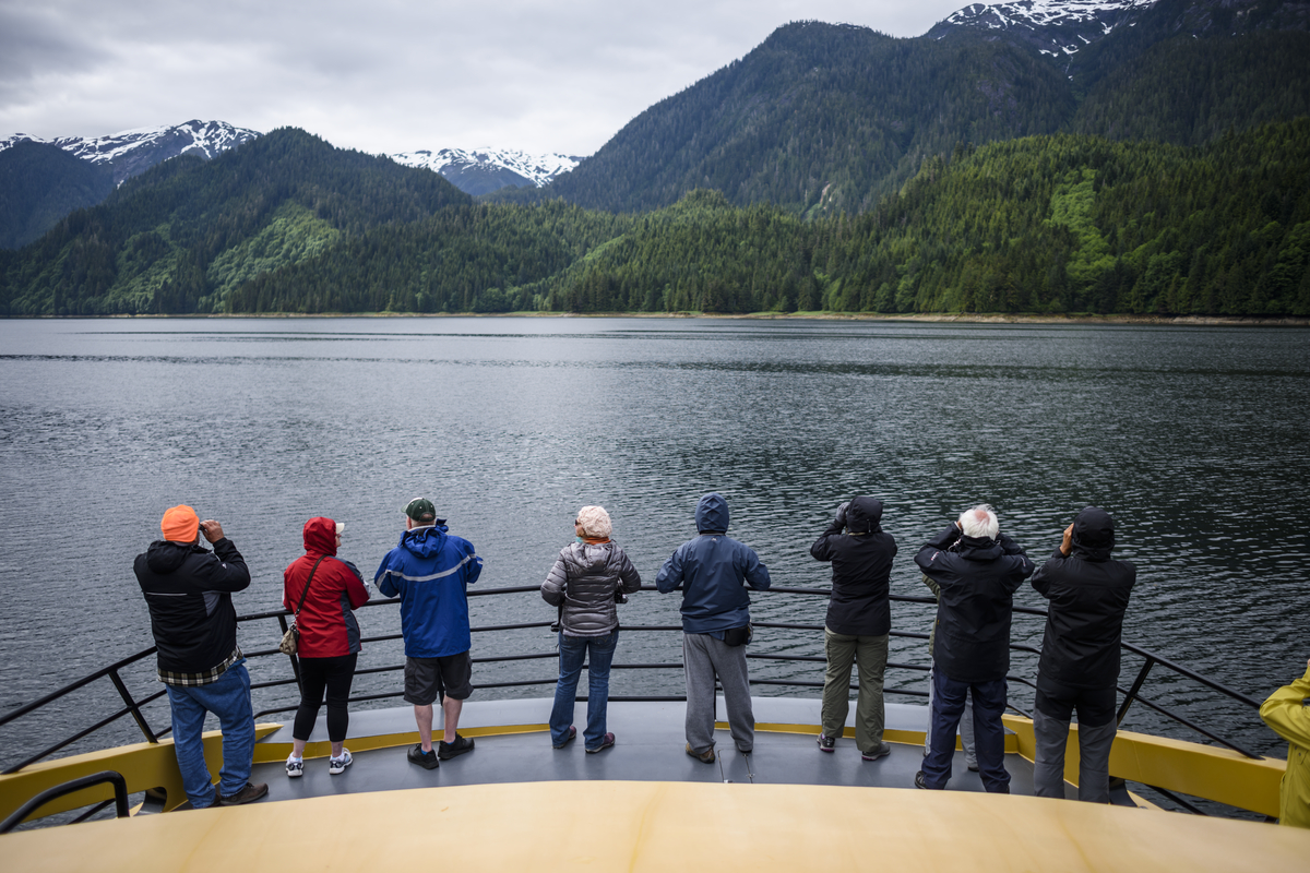 A group of adults look out on the back of a boat at the inlet