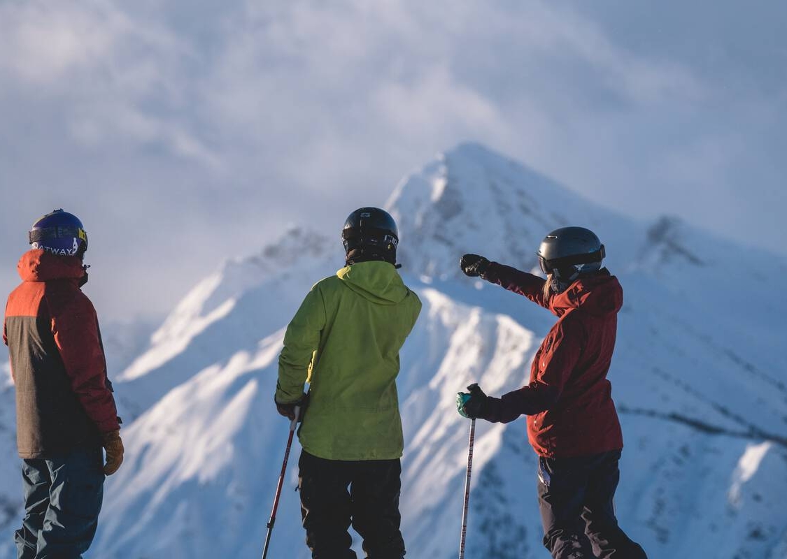 Un trío de esquiadores y practicantes de snowboard disfrutando de la vista desde la cima de una montaña en Kicking Horse Mountain Resort.