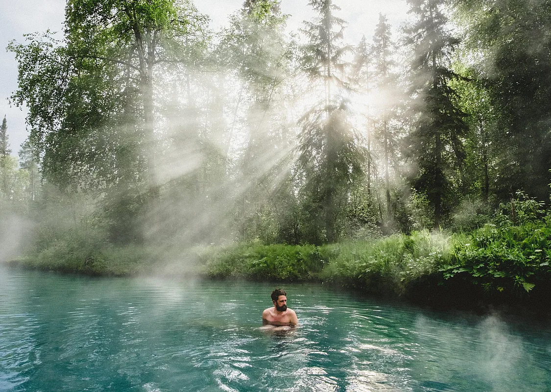 A person soaks in Liard hot springs with light rays peeking through the trees.