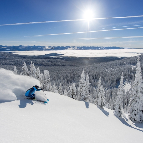 A skier takes large, sweeping powder turns on a bluebird day at Big White Ski Resort.