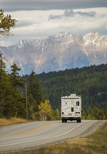 An RV drives away down a highway towards the mountain
