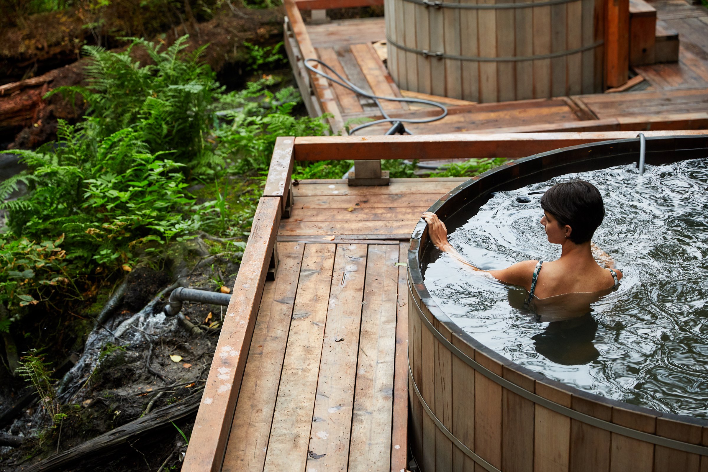A person in a wooden tub looks out at the hot springs over a viewing platform.