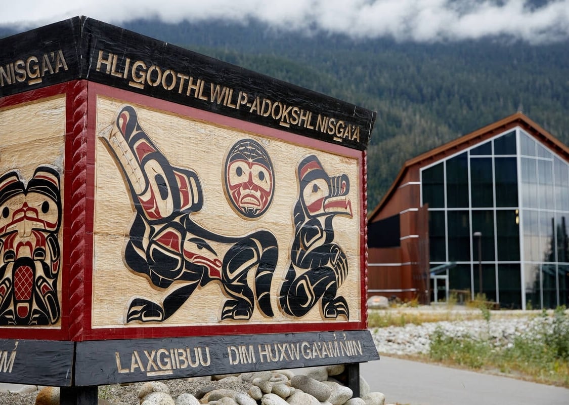 Ein Schild mit Nisga'a-Kunstwerken führt zu einem schönen Holzgebäude mit bodentiefen Fenstern, das den Blick auf den Nisga'a Lava Beds Provincial Park freigibt.