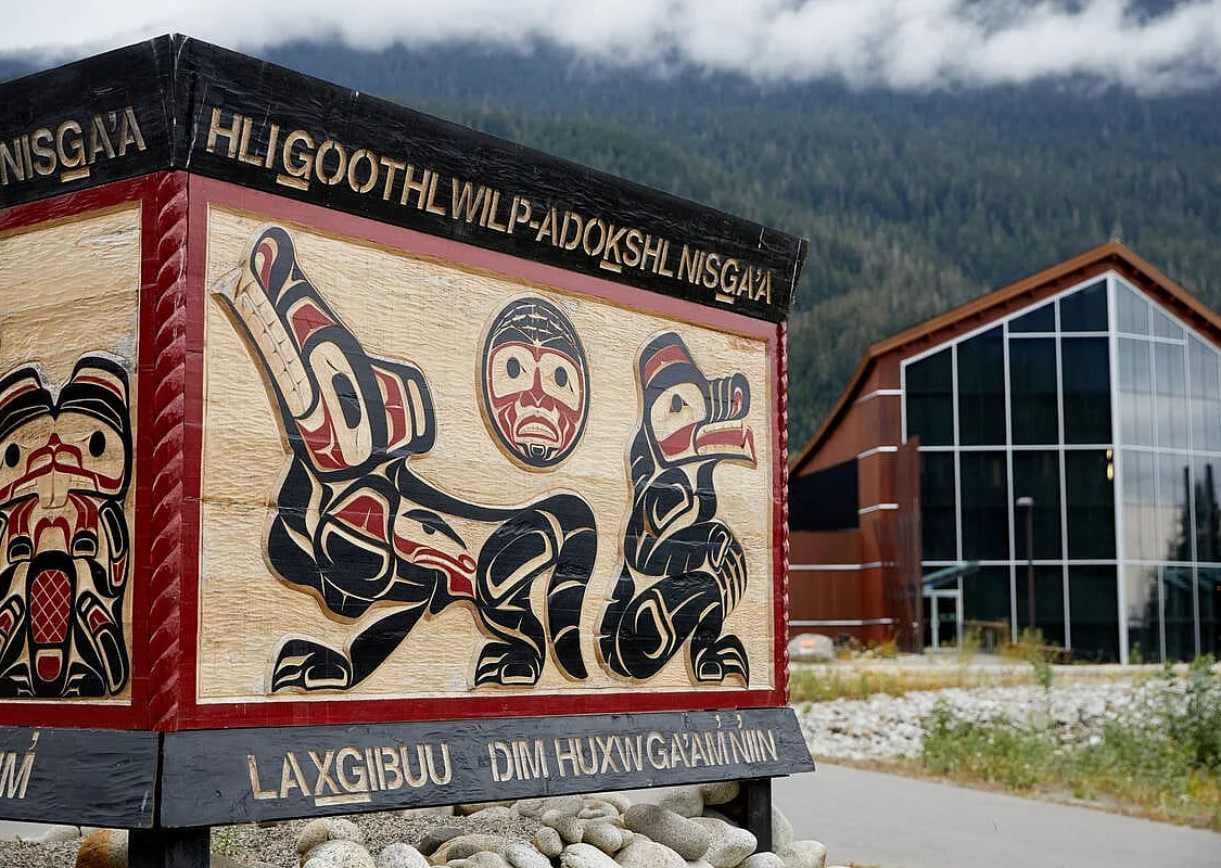 Ein Schild mit Nisga'a-Kunstwerken führt zu einem schönen Holzgebäude mit bodentiefen Fenstern, das den Blick auf den Nisga'a Lava Beds Provincial Park freigibt.