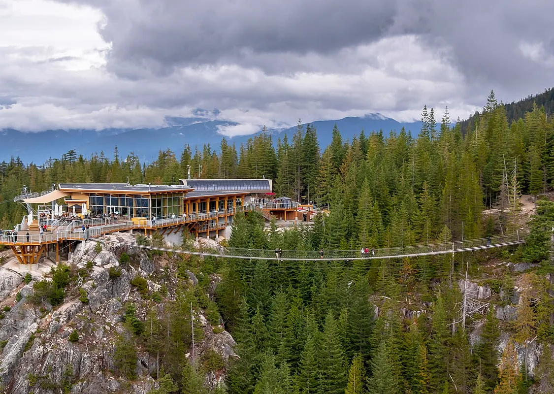 A view of the top building at the Sea to Sky Gondola and the suspension bridge with people walking across.