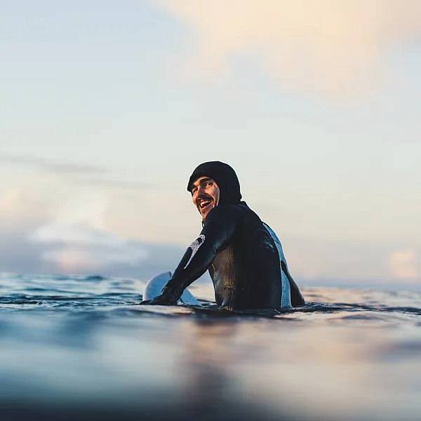 Un surfista con un traje de neopreno negro mira a la cámara desde el agua.