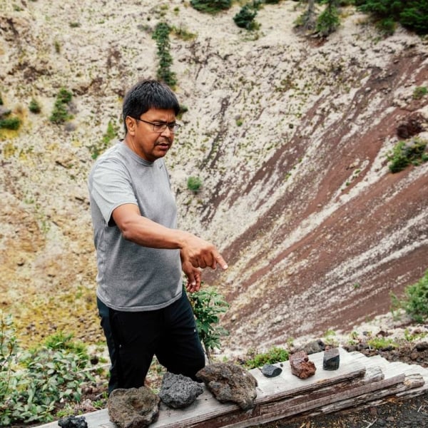 Un guía de las Primeras Naciones da una charla frente a un cono de lava, señalando rocas volcánicas.