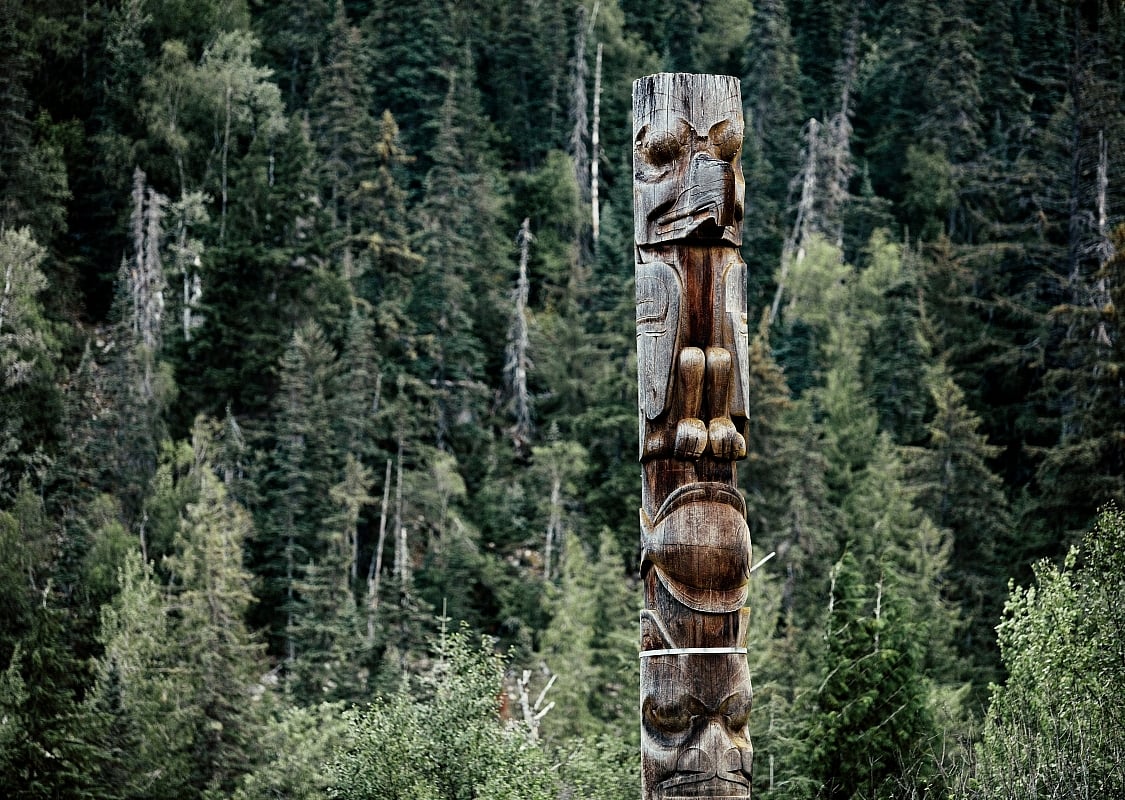 Ein alternder hölzerner Totempfahl steht hoch in einem Waldgebiet, im Dorf Gitwinksihlkw oder New Aiyansh, Teil der Nisga'a Nation.