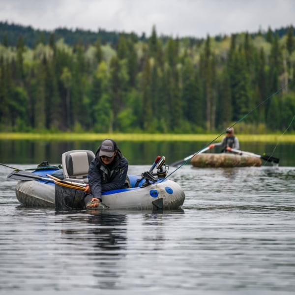 Two people float on Canim Lake in small fishing dingy's with fishing gear in the boats.