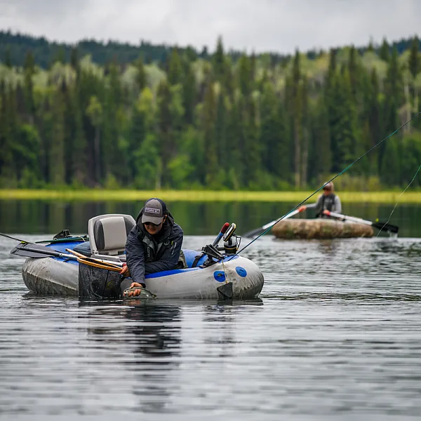 Two people float on Canim Lake in small fishing dingy's with fishing gear in the boats.