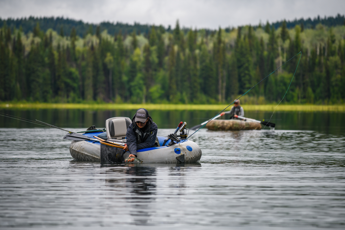 Two people float on Canim Lake in small fishing dingy's with fishing gear in the boats.