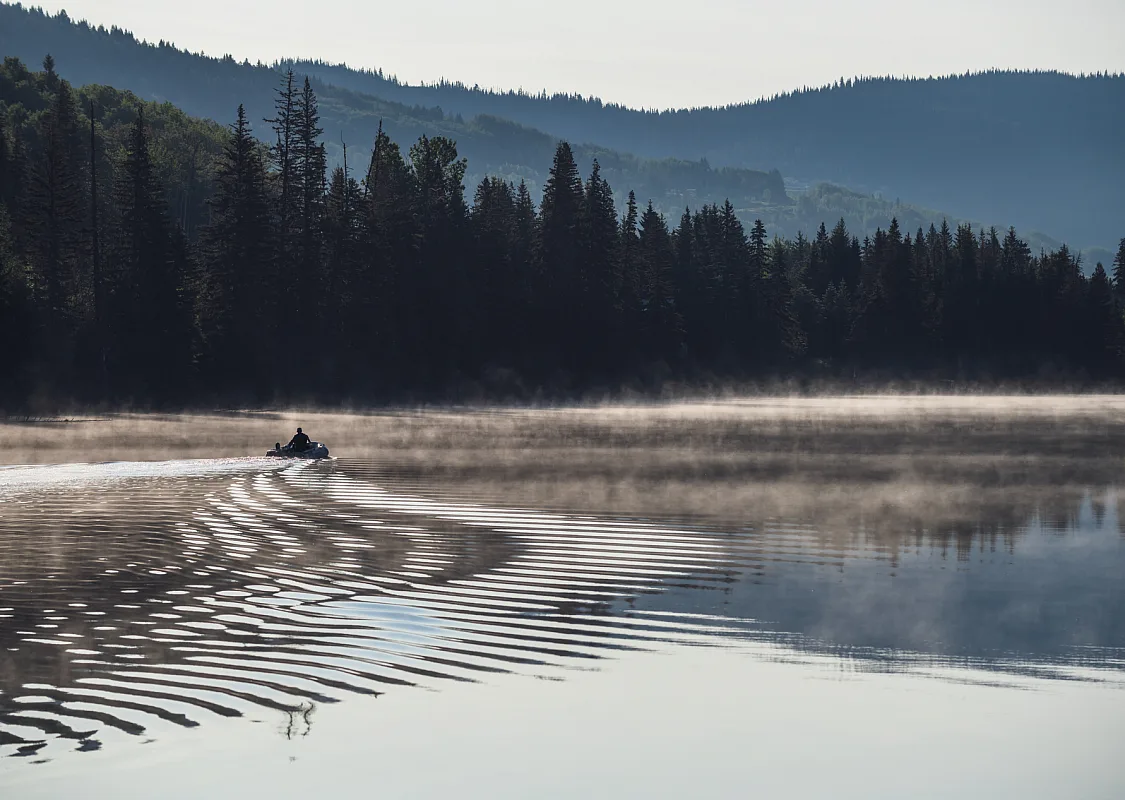 A boat heads out fishing on a misty morning on Lac des Roches