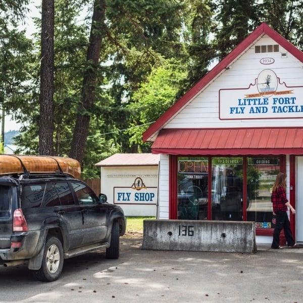 The outside of Little Fort Fly & Tackle shop. A car with a canoe strapped to the roof is parked out front of the store.