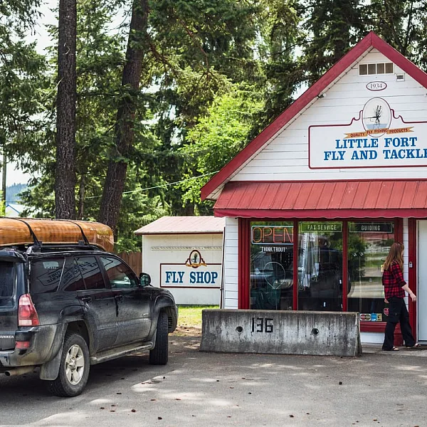 The outside of Little Fort Fly & Tackle shop. A car with a canoe strapped to the roof is parked out front of the store.