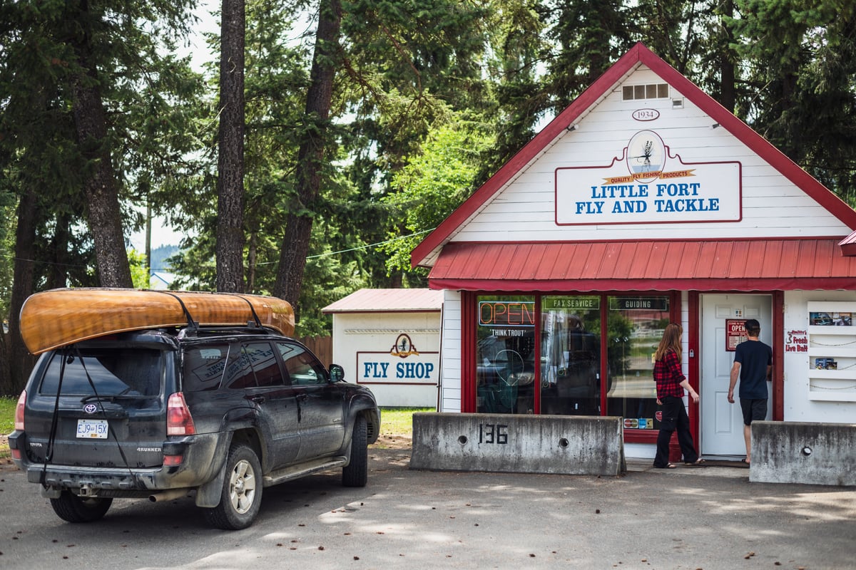 The outside of Little Fort Fly & Tackle shop. A car with a canoe strapped to the roof is parked out front of the store.