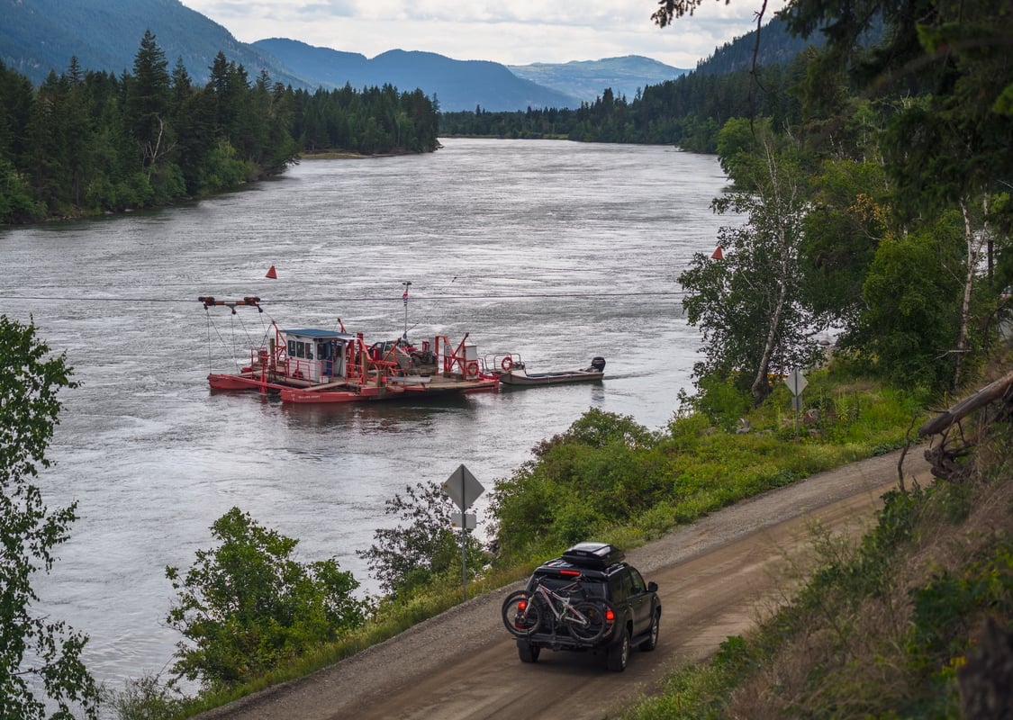 The McLure Ferry crossing the North Thompson River next to the highway as a car passes by.