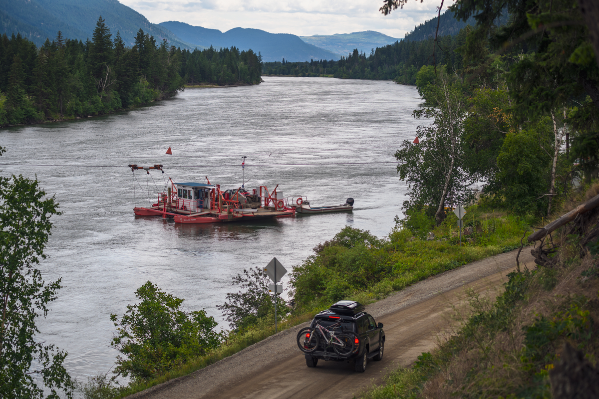 The McLure Ferry crossing the North Thompson River next to the highway as a car passes by.