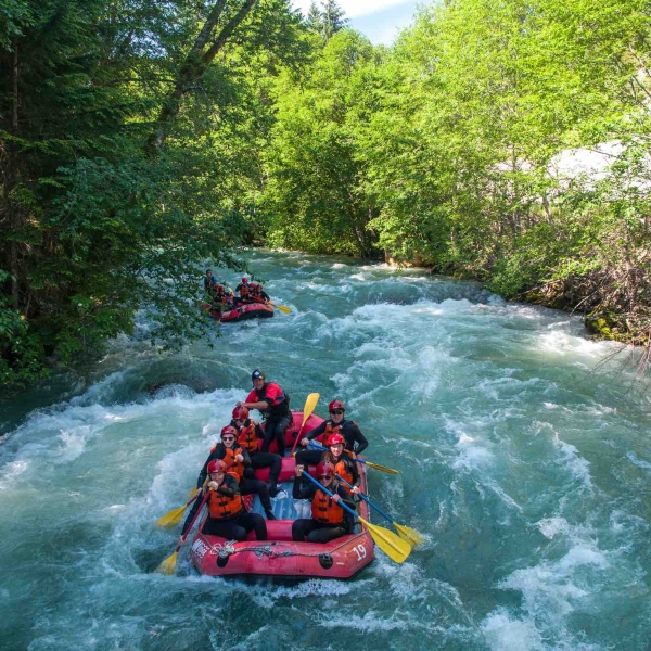 Two red rafts are paddled down a moving river in Whistler. Each raft has a guide and up to 8 eight rafting guests.