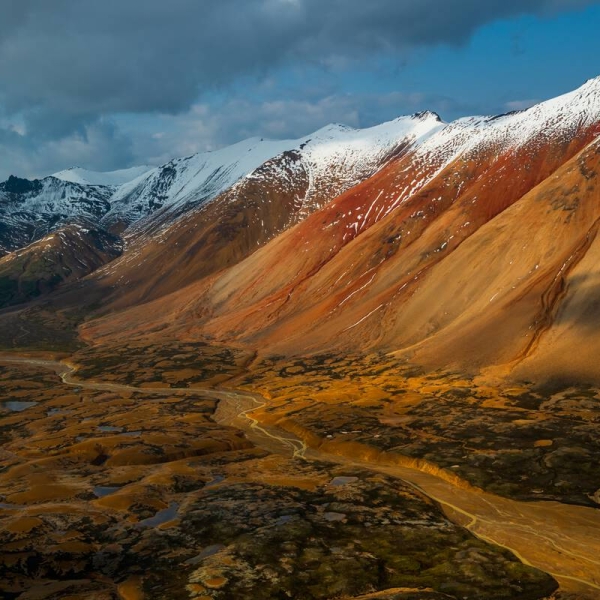 Snow covers the peaks of rust-coloured mountains in Mount Edziza Provincial Park.