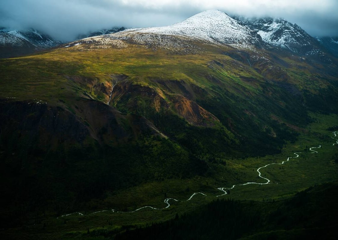 Una vista aérea de un exuberante valle fluvial rodeado por un mosaico de coloridas montañas cubiertas de nieve.