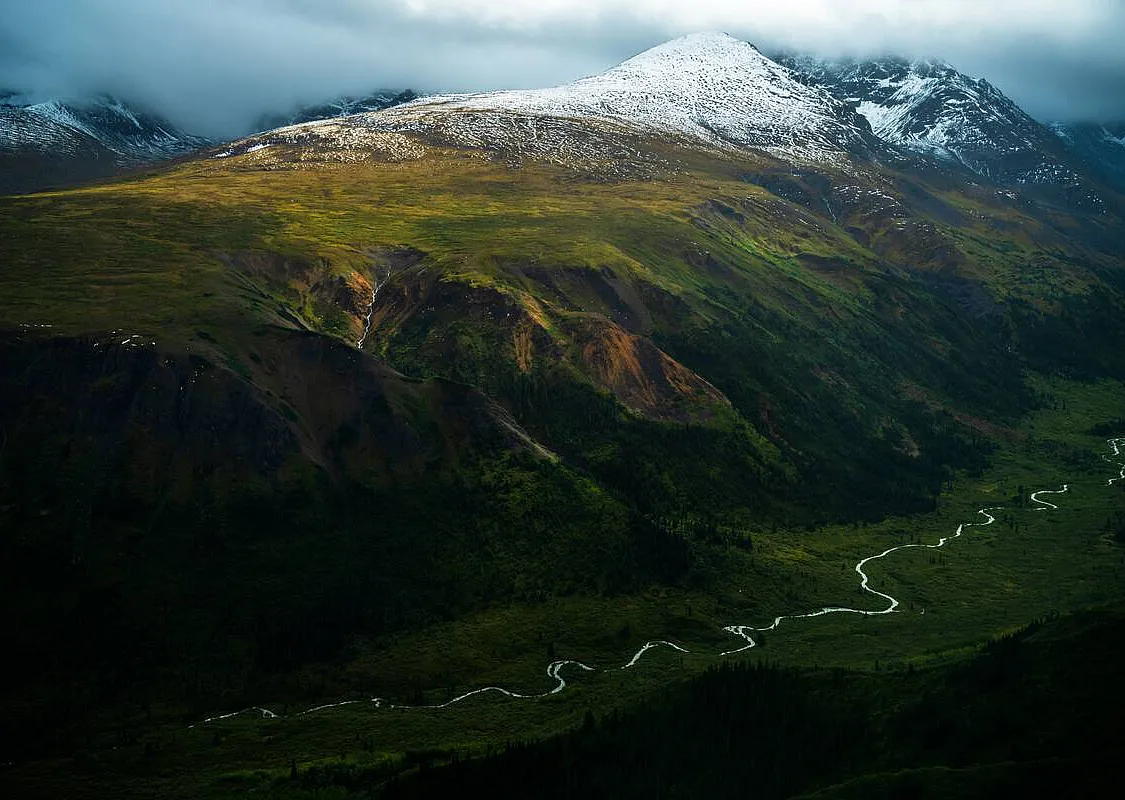 Una vista aérea de un exuberante valle fluvial rodeado por un mosaico de coloridas montañas cubiertas de nieve.