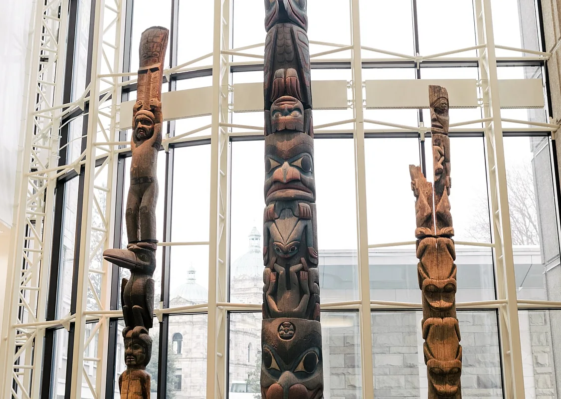 One person in a wheelchair and another stare up at a collection of Totem poles at the Royal BC Museum