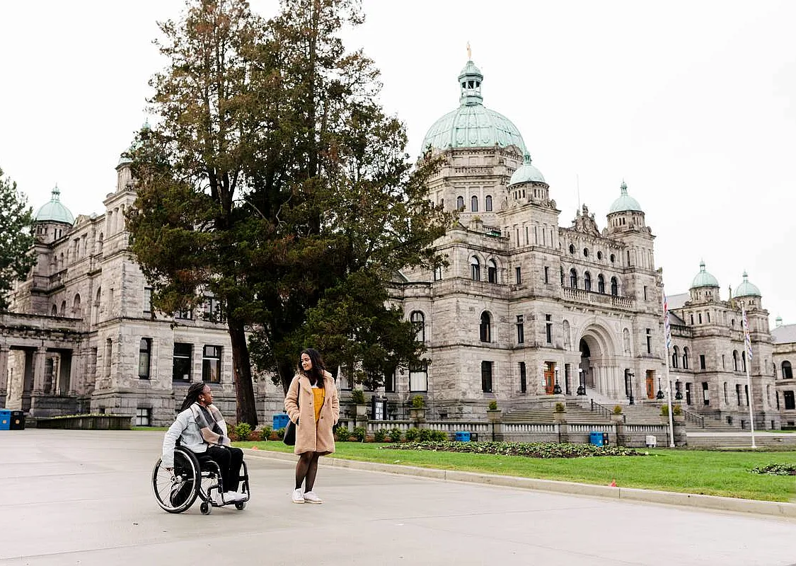One wheelchair user and another person move along the path in front of Parliament in Victoria