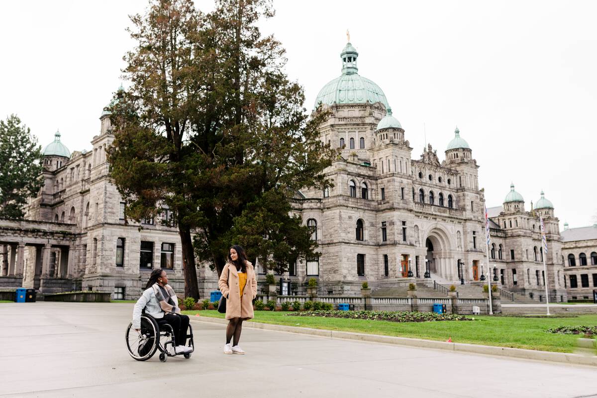 One wheelchair user and another person move along the path in front of Parliament in Victoria