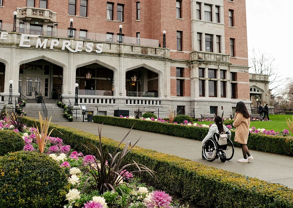 Dos personas se acercan al Fairmont Empress en Victoria. Se ven jardines de flores en primer plano.