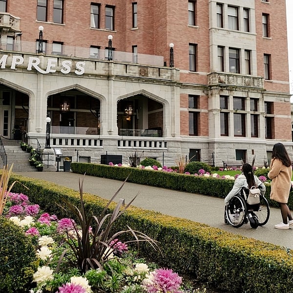 Two people approach the Fairmont Empress in Victoria. Flower gardens are seen in the foreground.